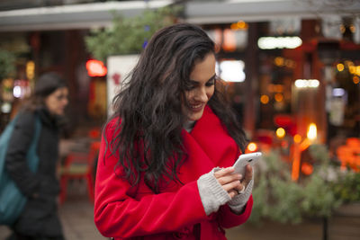 Smiling young woman using mobile phone while standing on city street
