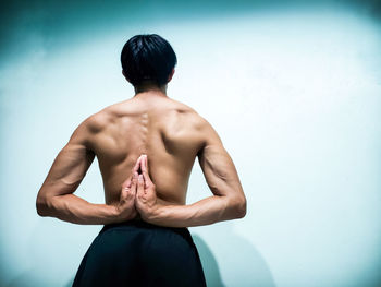 Rear view of shirtless man with hands behind back while standing against wall