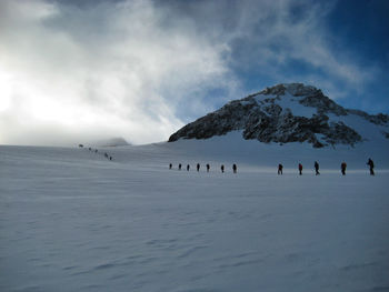 Scenic view of people walking on snow covered mountains against sky