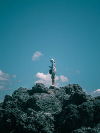 Man standing on rock against blue sky