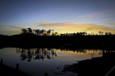 Silhouette trees by lake against sky during sunset