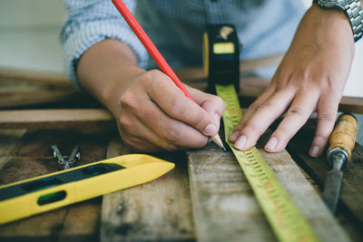 Midsection of carpenter measuring wood