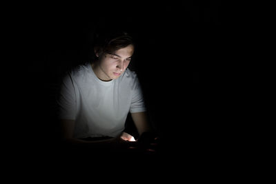 Young man with illuminated mobile phone sitting in darkroom