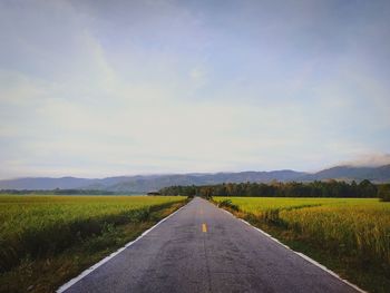 Empty road amidst field against sky