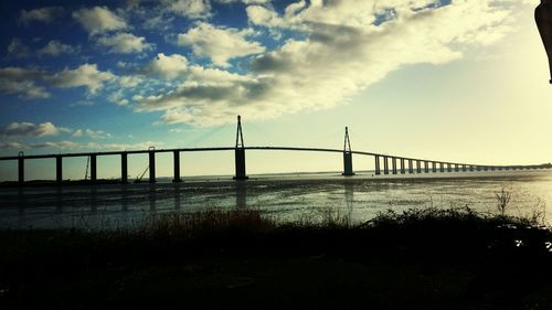 Bridge over river against cloudy sky