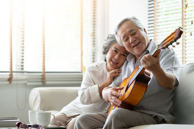 Happy senior couple playing guitar while sitting on sofa at home