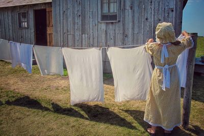 Rear view of woman drying clothes in back yard