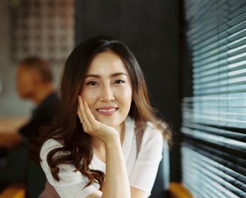 Portrait of smiling mid adult woman with hand on chin sitting in restaurant