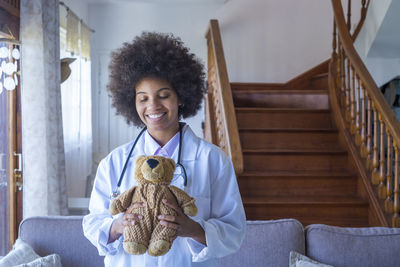 Smiling doctor holding teddy bear at home