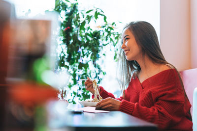 Beautiful smiling young asian woman in red clothes eating asian food in chinese restaurant