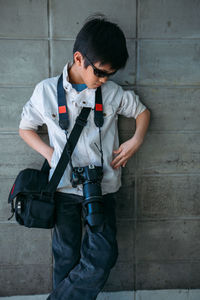 Cute boy with camera and bag posing against wall