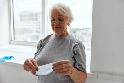 Mid adult woman standing against window at home