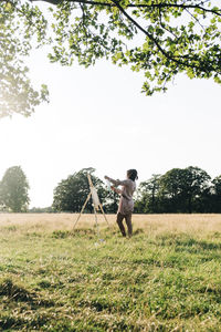 Mid adult woman checking painting while standing on grass