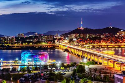 Aerial view of illuminated buildings by river in city at night