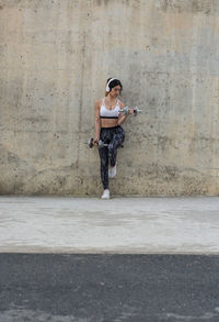 Young woman lifting dumbbells against concrete wall