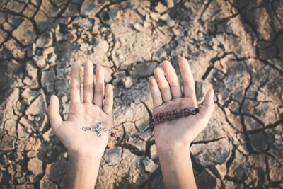 Cropped hands of woman holding rosary over ground