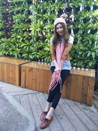 Full length portrait of smiling woman sitting against plants