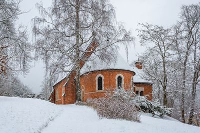 Bare trees by snow covered houses against sky during winter