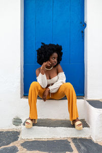 Full length of young woman sitting against door