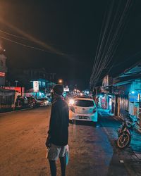 Rear view of man standing on illuminated road at night