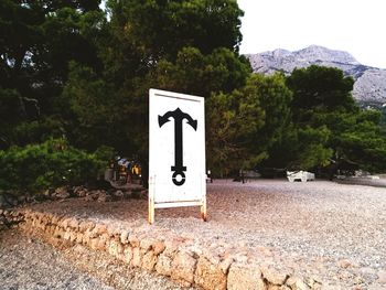 Road sign by trees against sky