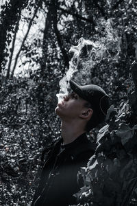 Man exhaling smoke while standing in forest