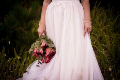 Midsection of bride wearing wedding dress standing on field