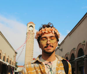 Portrait of young man with eye makeup and flower crown behind historic old clock tower adana turkey