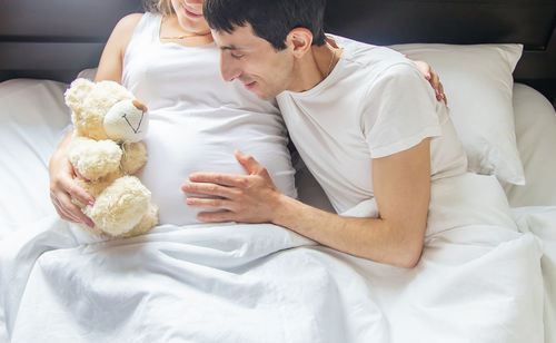 High angle view of man touching belly of pregnant woman while lying in bed