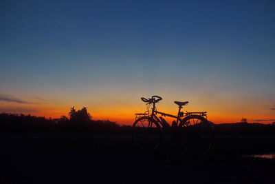 Silhouette bicycle on land against sky during sunset