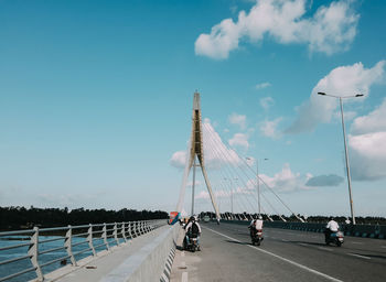 People on street with bridge against cloudy sky