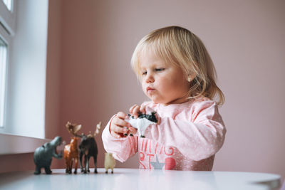 Little girl toddler in pink playing with animal toys on table in children's room at home