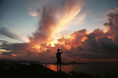 Silhouette of man standing on beach against cloudy sky