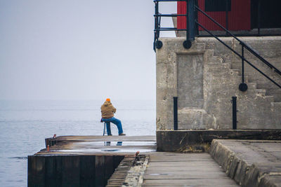 Full length rear view of man sitting on chair at pier