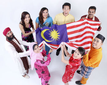 High angle portrait of happy friends holding malaysian flag over white background