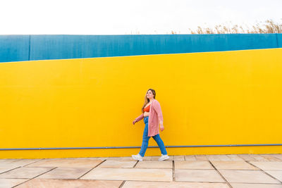 Full length of young woman walking against wall