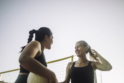 Low angle view of happy female friends talking while playing volleyball against sky