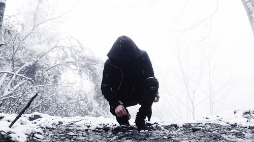 Man in hooded clothing crouching on snow covered field