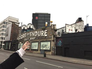 Person on road sign against buildings in city against sky