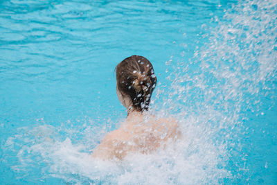 Rear view of teenage girl splashing water in swimming pool