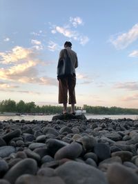 Rear view of man standing on rocks at sunset