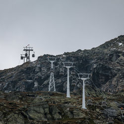 Low angle view of overhead cable cars on rocky mountain against sky