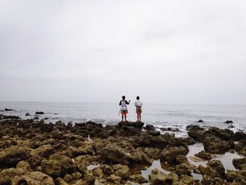 Rear view of boys standing on rocks at sea shore