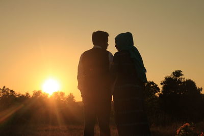 Rear view of man and woman standing against sky during sunset