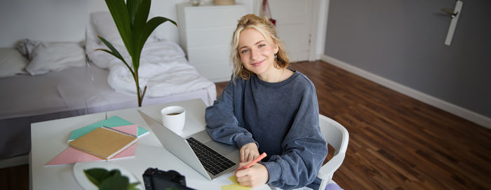 Portrait of young woman using digital tablet while sitting on table
