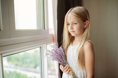Girl looking through window holding lavender