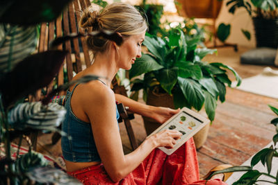 A female florist is sitting in a studio working on a tablet and shopping online.