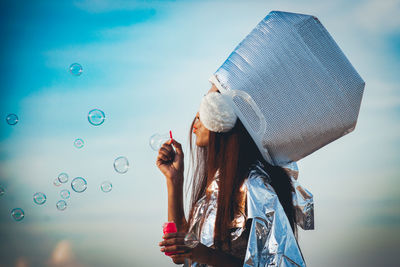 Woman wearing hat blowing bubbles against sky