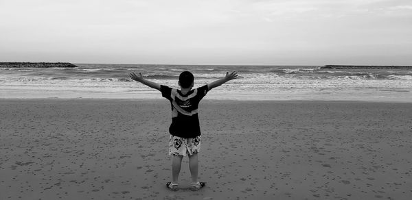 Rear view of man standing at beach against sky