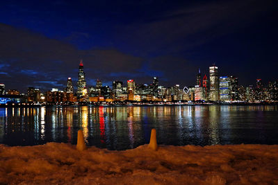 Illuminated cityscape by river at night